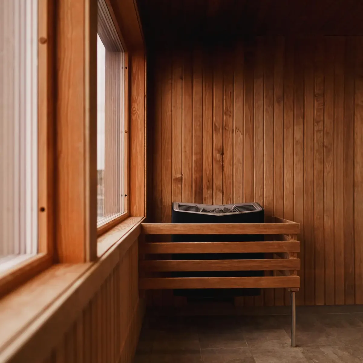 Holzsauna-Innenraum mit Fenster und elektrischem Ofen auf gefliestem Boden.